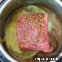 An easy Instant Pot corned beef and cabbage dish comes together as an uncooked, seasoned brisket mingles with fresh cabbage and onions in a savory broth, ready to be transformed into a delicious meal.