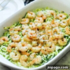 Baked lemon garlic shrimp on zoodles in a white casserole dish, garnished with herbs.