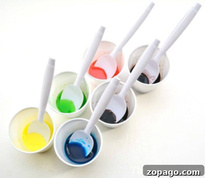 Fruity Scented Art 4 Six spoons rest in white cups filled with vibrant Kool-Aid-colored liquids: yellow, green, blue, red, teal, and purple, arranged on a white background.