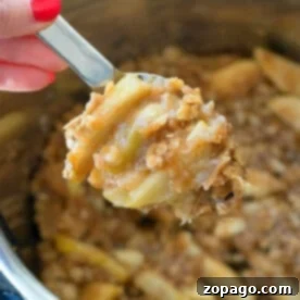 Effortless Instant Pot Apple Crisp 6 A hand holding a spoonful of delicious instant pot apple crisp from a pot.