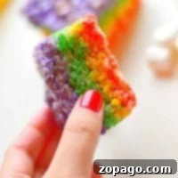 A hand holds a vibrant rainbow rice krispy treat, revealing a tempting bite taken out of its colorful layers.