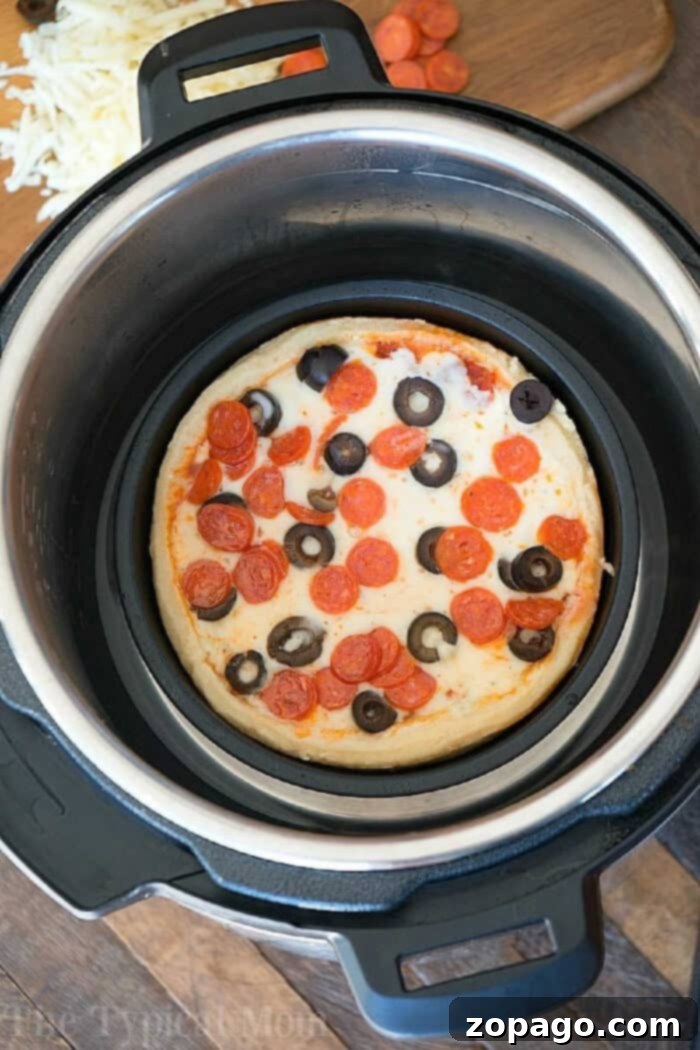Easy Instant Pot Pizza 6 A personal-sized pepperoni and black olive pizza, perfectly cooked, sits inside an Instant Pot, with fresh pizza toppings artfully arranged on a cutting board in the background.