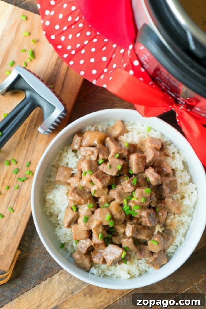 Instant Pot cube steak with gravy is yummy! Tender bites of meat smothered in a creamy mushroom sauce. A total winner. #instantpot #pressurecooker #cubesteak #steak #thetypicalmom #instantpotrecipes A bowl of savory beef steak with rice, garnished with chives, sits invitingly next to a meat tenderizer and an Instant Pot—perfect for when youre craving that cube steak tenderness.