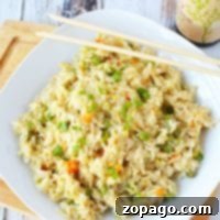 A plate of pressure cooker fried rice with peas and carrots rests on a wooden board, accompanied by chopsticks and a bottle of soy sauce.