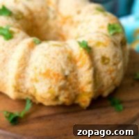 A bundt-shaped savory beer bread rests on a wooden board. The bread is lightly browned with small visible chunks of cheese and herbs.
