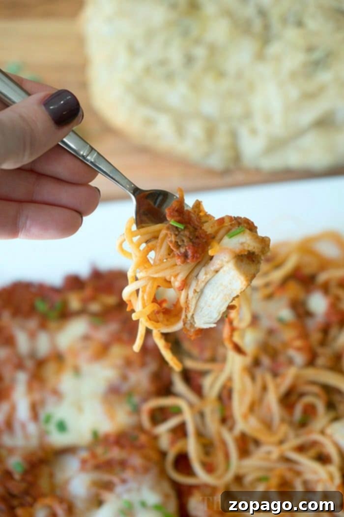 Warm & Fluffy Slow Cooker Rolls 6 Close-up of a fork holding spaghetti and chicken over a plate of pasta, with freshly baked slow cooker rolls in the background.