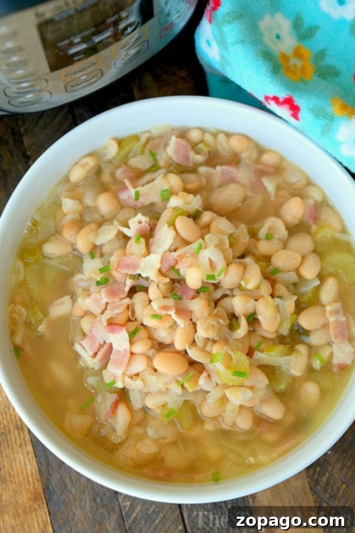 Healthy and homemade pressure cooker bean soup, perfect for your Instant Pot all year long. #pressurecooker #instantpot #crockpotexpress #bean #soup #northernbeans #healthy #instantpotrecipes #thetypicalmom #beansoup A steaming bowl of pressure cooker bean soup, generously topped with crispy bacon bits and fresh herbs, sits on a rustic wooden table beside a patterned kitchen cloth.