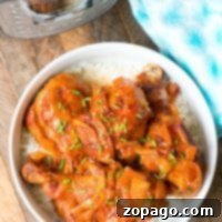 A bowl of delicious chicken legs with onions and sauce on a bed of rice sits invitingly next to an Instant Pot, showcasing tender chicken legs. The cozy scene is completed with a blue towel on the rustic wooden surface.