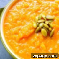 Creamy Butternut Carrot Delight 4 Bowl of dairy-free butternut squash soup topped with green pumpkin seeds, showing a spoonful being lifted.