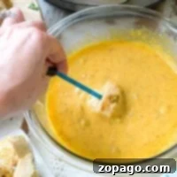 A bowl of yellow cheese fondue with broccoli invites a hand to dip a piece of bread using a blue fork. An Instant Pot pressure cooker sits in the background, while a plate with bread chunks waits on the side.