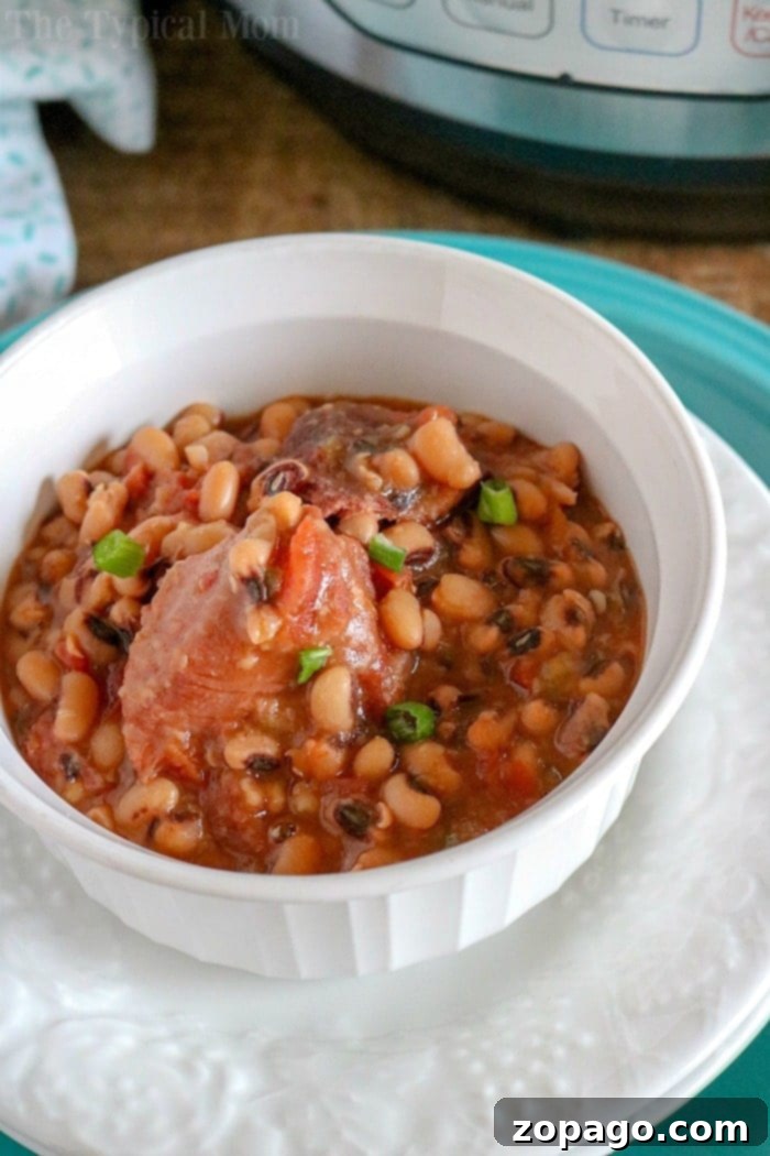 Hearty Instant Pot Black Eyed Peas and Ham: An easy and healthy no-soak recipe for pressure cooker or slow cooker, ideal for leftover ham. Serve as a comforting meal for any occasion. Close-up of a rustic white bowl filled with Black Eyed Peas and Ham, garnished with fresh green herbs. The hearty stew is served on a dark wooden surface with a spoon.