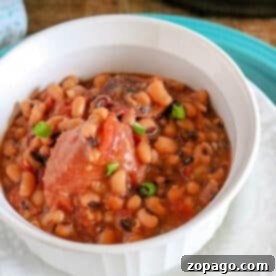 A white bowl filled with pressure cooker black eyed peas and ham in broth, garnished with green onions.