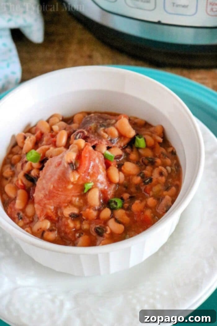 Black Eyed Peas and Ham Hocks: A Southern Comfort Classic 5 A white bowl filled with pressure cooker black eyed peas and ham in broth, garnished with fresh green onions and a slice of cornbread on the side, served on a rustic wooden table.
