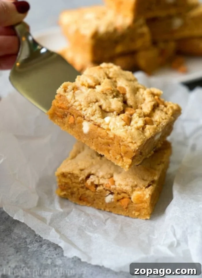 Decadent Peanut Butter Cake Mix Brownies 2 A spatula lifts a square cake mix peanut butter brownie stuffed with peanut butter chips, placed on parchment paper, highlighting its gooey texture and generous chocolate chips.