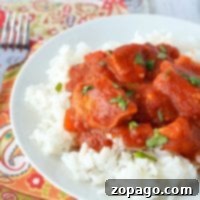 A vibrant plate of rice topped with a tangy tomato sauce and fresh herbs sits elegantly on a patterned tablecloth, reminiscent of the flavors in a hearty, healthy butter chicken recipe. Nearby, a gleaming fork waits to savor every delightful bite.
