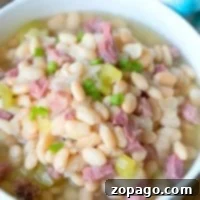 A bowl of pressure cooker ham and beans soup with chunks of ham, celery, and green onion on top.