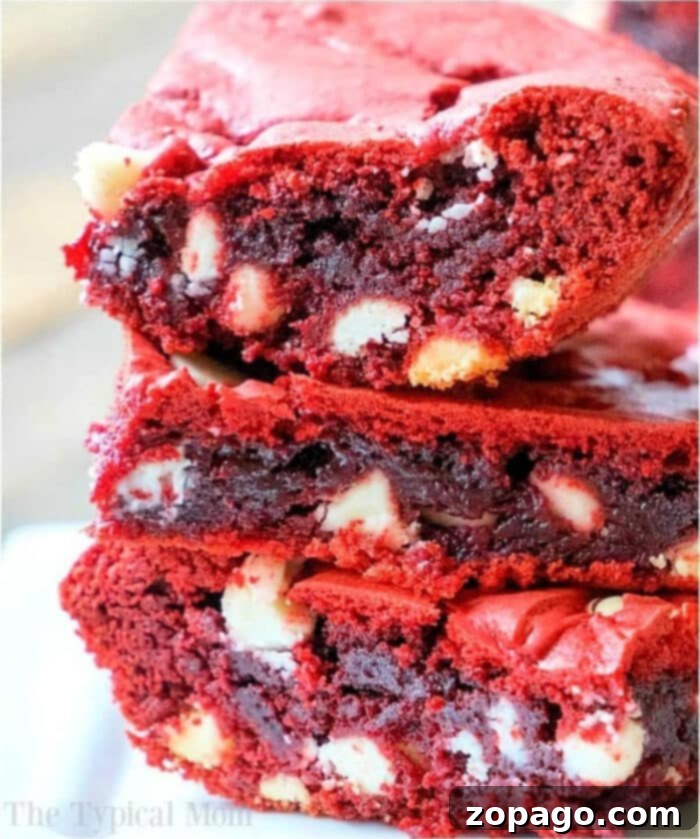 Shortcut Red Velvet Brownies 2 Close-up of three decadent red velvet brownies made from cake mix, neatly stacked to reveal a dense, rich texture studded with visible white chocolate chips and a vibrant red hue.