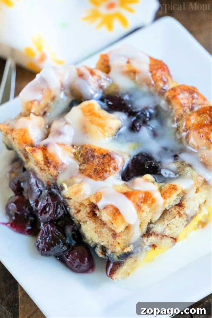 Gooey Cinnamon Roll Bake 2 Pillsbury Cinnamon Roll Breakfast Casserole with blueberries, glistening with icing, ready for serving.