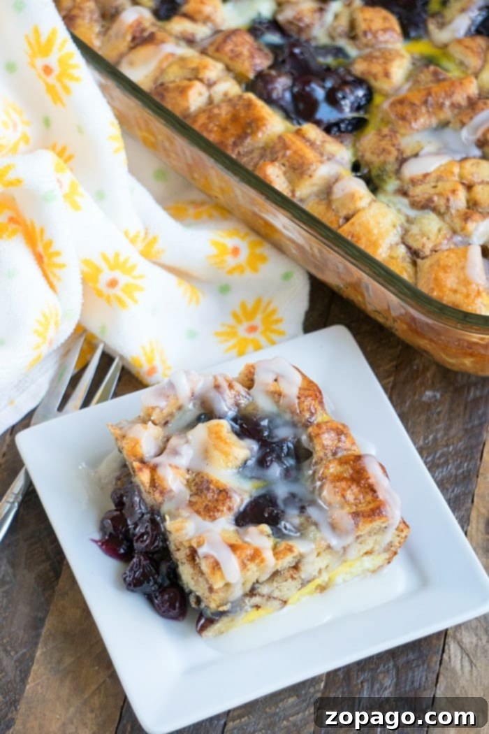 This easy cinnamon roll breakfast casserole with blueberries is just amazing! Served for brunch or on Christmas morning it is a great way to make cinnamon rolls into a fruit casserole that everyone will love. Feeds 12 and costs under $10 to make which is a winner in my book! #cinnamonroll #casserole #breakfast #blueberry #fruit #easy A slice of Cinnamon Roll Breakfast Casserole, showcasing its layers and sweet glaze, ready to eat.
