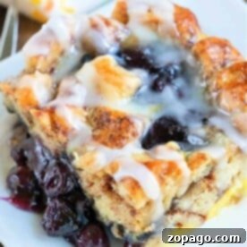 A glazed blueberry pastry on a white plate, with layers of bread and visible cherry filling, evokes the comforting warmth of a cinnamon roll—a delightful breakfast casserole treat.