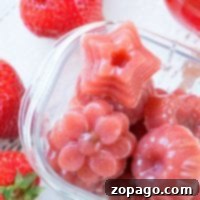 Homemade fruit snacks in star and flower shapes, these strawberry gummies come in a clear container, surrounded by fresh strawberries.