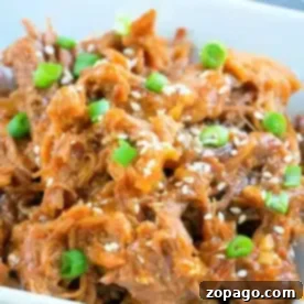 A white rectangular dish filled with Asian Instant Pot pulled pork, garnished with sliced green onions and sesame seeds. The shredded meat appears to be coated in a savory sauce.