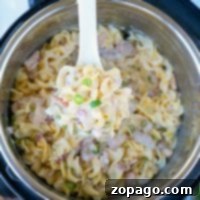 A hand serves creamy pasta with peas and bacon from an Instant Pot, reminiscent of the flavors found in a crack chicken casserole.