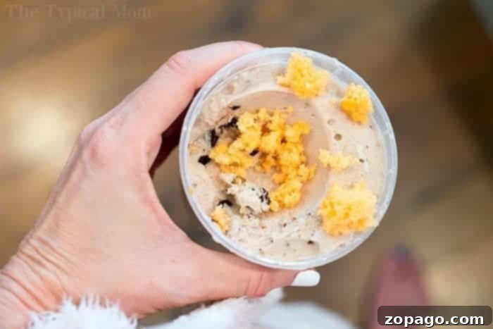 Pop-Infused Cupcakes 4 A person holding a clear plastic cup filled with a creamy dessert and topped with crumbled pieces of orange-flavored 2-ingredient soda cake, showcasing a creative way to serve the cake.