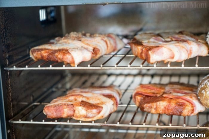 These smoked bacon wrapped pork chops are incredible and you have to make them tonight! Pair with our smoked baked potatoes for the perfect meal. #smoked #smoker #porkchops #bacon #pork #rub #smokerrecipes smoked pork chops, bacon wrapped