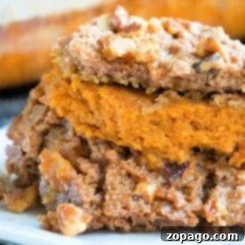 Close-up of a dessert slice with layers of pumpkin pie dump cake, crumbly topping, and walnuts on a white plate.
