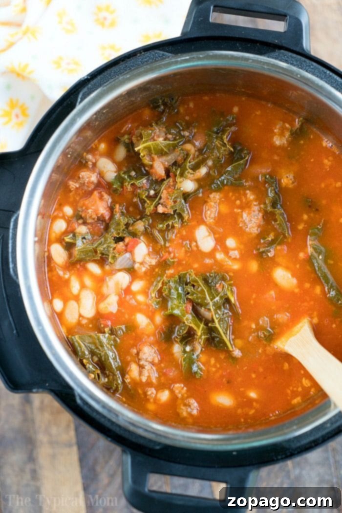 Pressure cooker sausage soup is packed with flavor and can be made with or without kale. Using canned or dry beans it's the perfect dinner. A close-up of a pressure cooker filled with savory sausage, white bean, and kale soup, ready to be served.