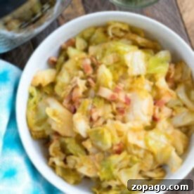 Bowl of pressure cooker fried cabbage with bacon pieces, next to a small bowl of chopped chives on a wooden table.