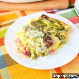 Creamy Asparagus Bake 3 A slice of vegetable asparagus egg casserole recipe, rests on a white plate atop a colorful plaid tablecloth.