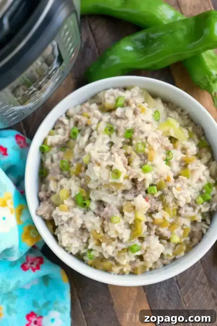Pressure Cooker Sausage Rice Casserole with Hatch Chiles A bowl of creamy Instant Pot sausage rice casserole garnished with chopped green onions sits on a wooden surface next to whole green peppers and a colorful floral kitchen towel. An Instant Pot is partially visible in the corner, hinting at the delicious simplicity of this comforting dish.