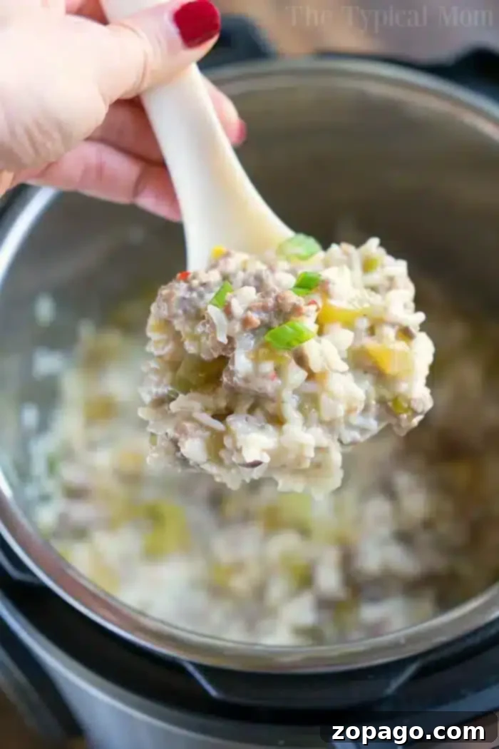 Serving Instant Pot Sausage Rice Casserole A hand holding a white spoon serves a portion of Instant Pot sausage rice casserole. The dish features creamy, seasoned rice blended with ground meat and green peppers, complemented by small vegetable pieces.
