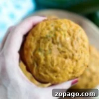Moist Pumpkin Zucchini Muffins 2 A hand holds a freshly baked pumpkin zucchini muffin, with a rustic wooden board in the background.