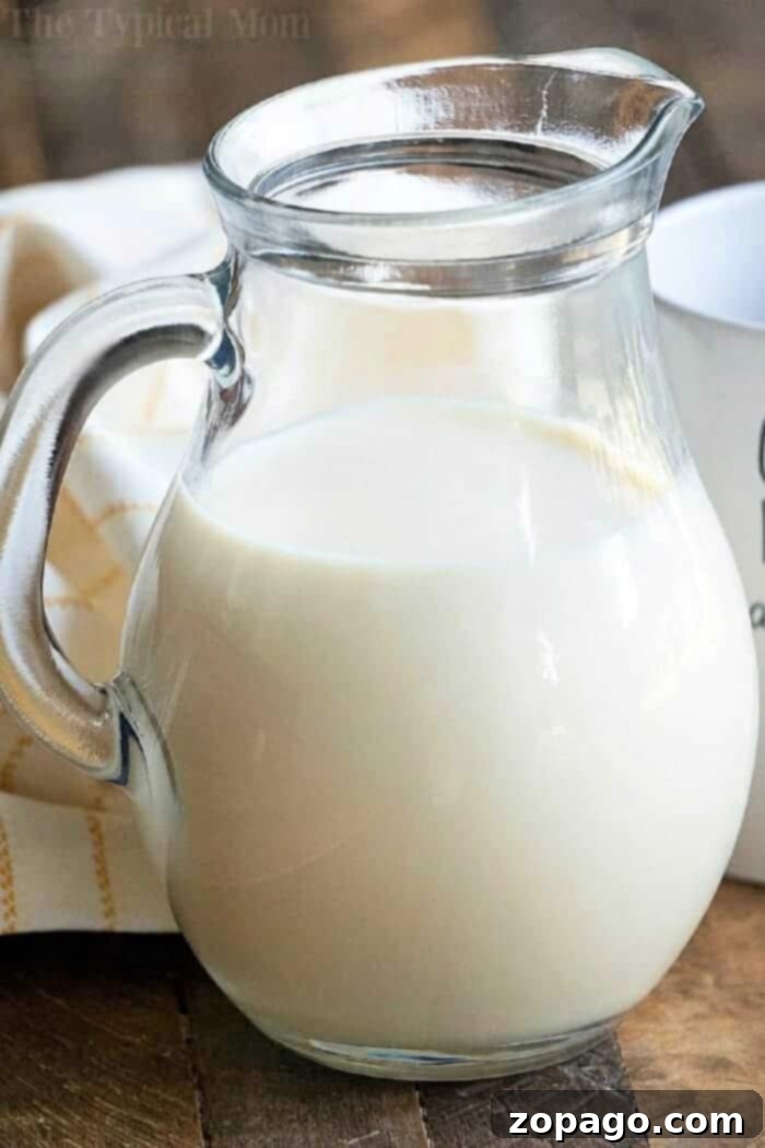 A clear glass pitcher filled with milk and pumpkin spice coffee creamer sits on a wooden table next to a white cloth, inviting a warm and cozy feeling.