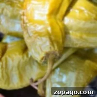 Close-up of roasted chiles with wrinkled skin and stems, arranged alongside smoked chiles on a grill.