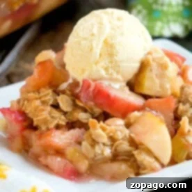 A delightful apple crisp topped with a scoop of vanilla ice cream rests on a white plate, accompanied by a floral napkin nearby. The subtle hint of rhubarb crunch adds an unexpected twist to this classic dessert experience.