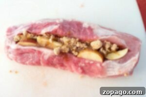 Raw pork loin meticulously sliced open and generously stuffed with sweet apple slices and rich brown sugar, laid out on a clean white cutting board, showcasing the meticulous preparation for your next smoked pork recipe.