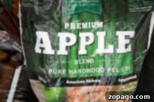 A bag labeled Premium Apple Blend from Green Mountain Grills, featuring 100% pure hardwood pellets, perfect for infusing a rich, fruity smoke into dishes like smoked beer can chicken. The design showcases a vibrant green woodgrain background with text highlighting the blend of American hickory and applewood.