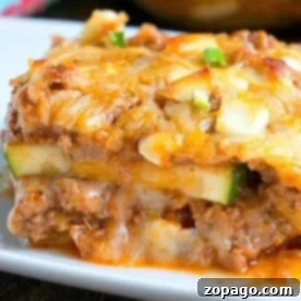 A close-up of a cheesy slice of no noodle zucchini lasagna on a white plate.