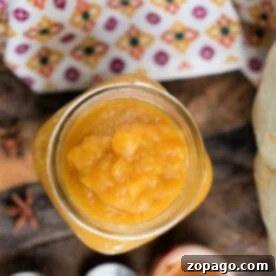 Top view of a jar filled with chunky applesauce on a wooden surface, next to a patterned cloth—perfect alongside homemade Instant Pot Pumpkin Butter.