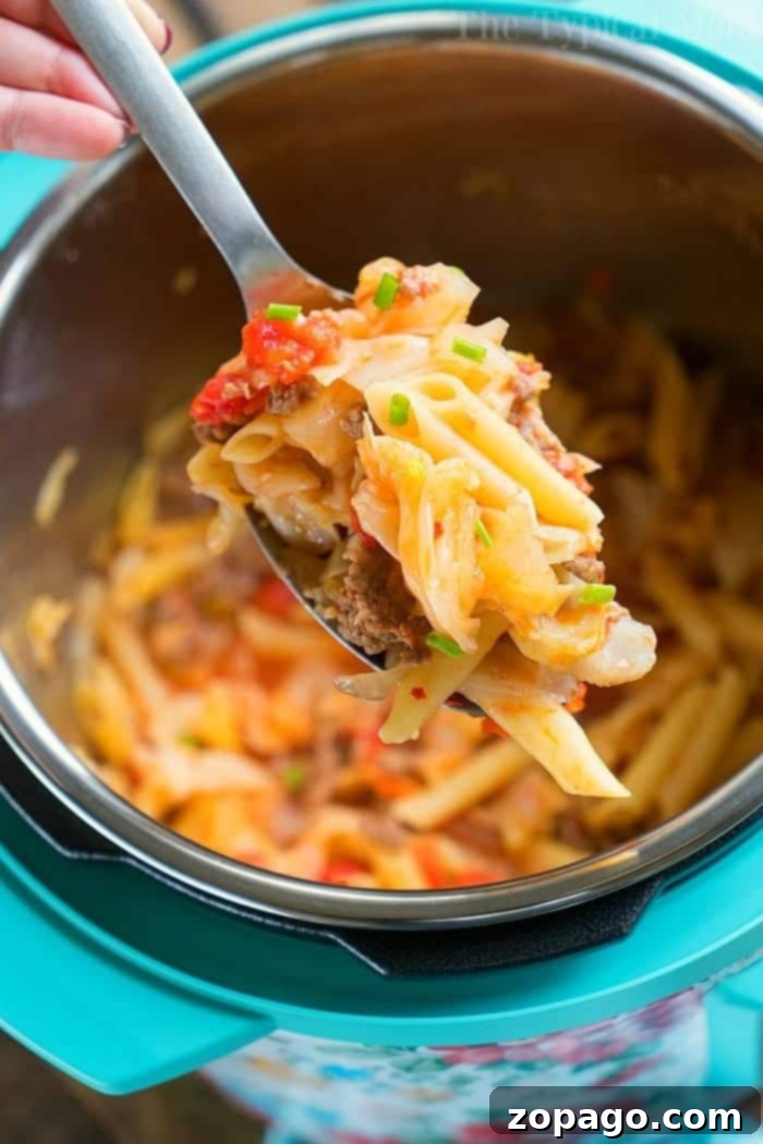 Instant Pot sausage and cabbage with noodles. #instantpot #sausage #cabbage #ninjafoodi #casserole A spoonful of cheesy pasta with ground meat, sausage, and vegetables is being lifted from an Instant Pot. This delightful pressure cooker dish includes penne, chopped tomatoes, cabbage, and garnished green onions. The interior of the pot is also visible.