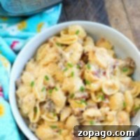 A hearty bowl of creamy macaroni and cheese loaded with bacon and sausage, garnished with fresh chives, ready to eat. An Instant Pot is in the background.