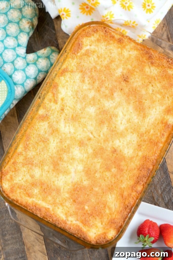 This 2 ingredient pineapple angel food cake recipe is a simple throw together dessert that's great when people come over unexpectedly. #angelfoodcake #pineapple #cake #dumpcake #weightwatchers #skinny #fruit #angelfood A golden-brown baked pineapple angel food cake recipe, rests in a glass dish. Nearby, a blue oven mitt and a plate with strawberries are artfully arranged on a wooden table.