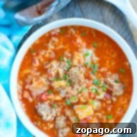 A bowl of hearty pressure cooker cabbage soup with ground meat, tomatoes, and rice sits next to a blue towel.
