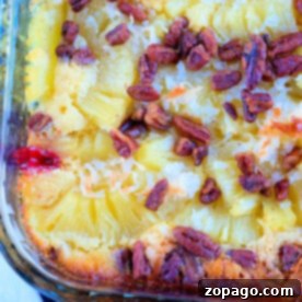 Close-up of cherry pineapple dump cake with white cake mix in a glass dish, showcasing layers of juicy pineapples, rich coconut, and crunchy pecans on top.