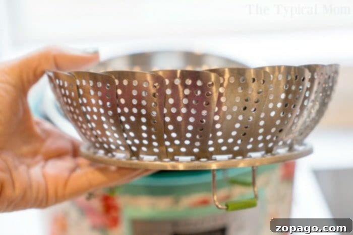 Enhance your Instant Pot's capabilities with a versatile steamer basket, perfect for vegetables, seafood, and more. A hand holds a metal folding steamer basket over a bowl, highlighting its perforated design and expandable form, a crucial Instant Pot accessory for healthy cooking.