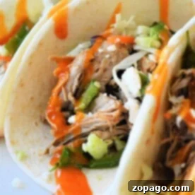 Close-up of Instant Pot tacos brimming with shredded meat, crisp lettuce, cheese, and a drizzle of hot sauce.